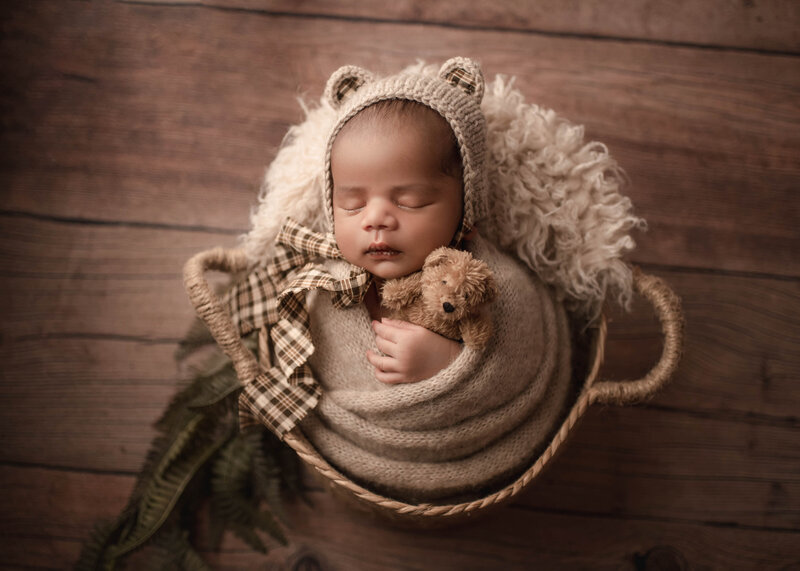 Baby boy wrapped in beige wearing bear bonnet holding tiny bear