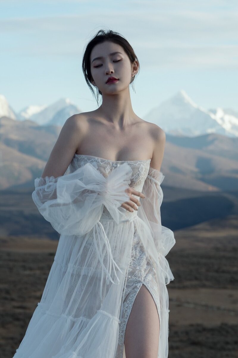 A beautiful woman wearing a couture bridal dress photographed in wild fields with snow capped mountains in the background.