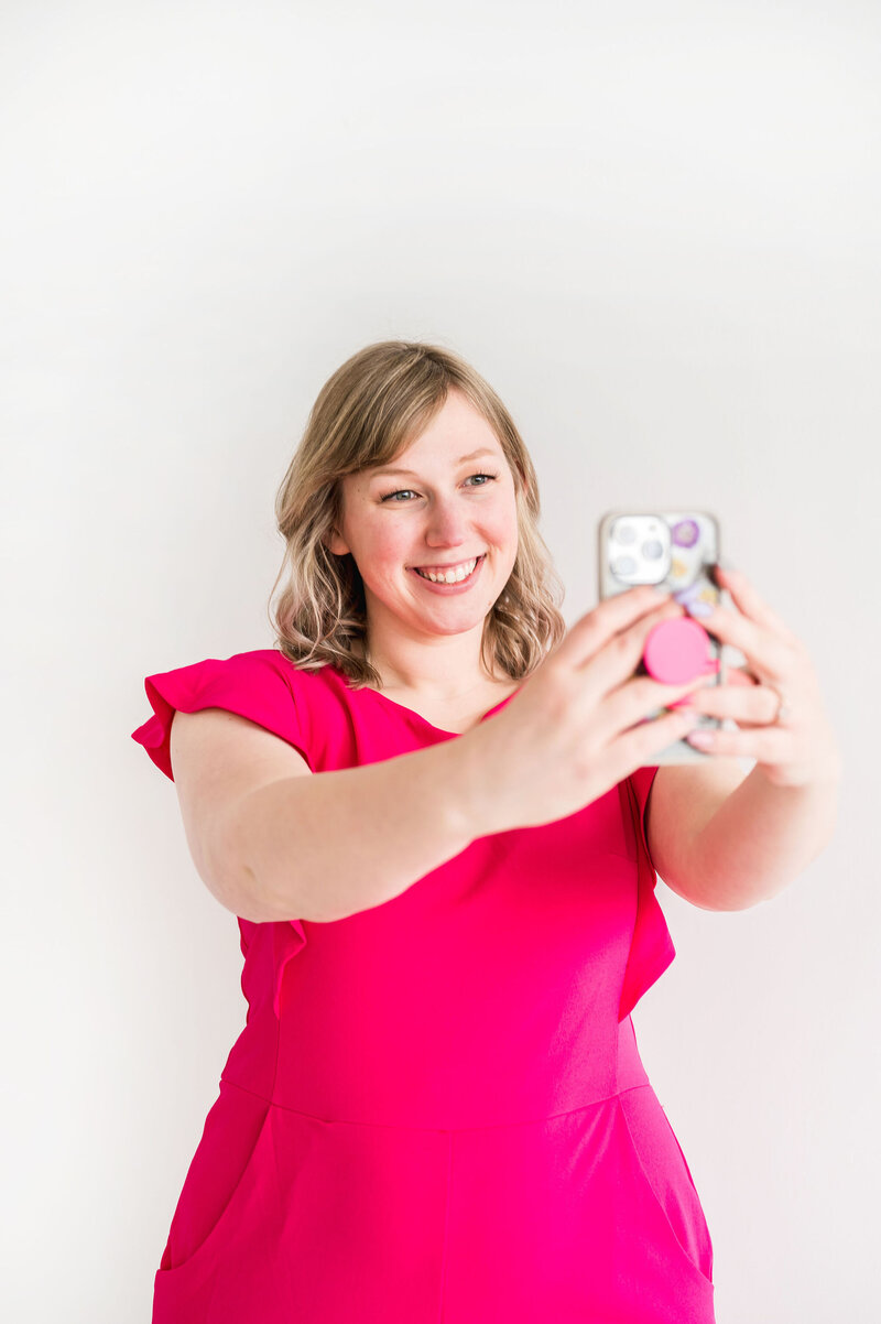 Kat Murphy in a pink jumpsuit taking a selfie