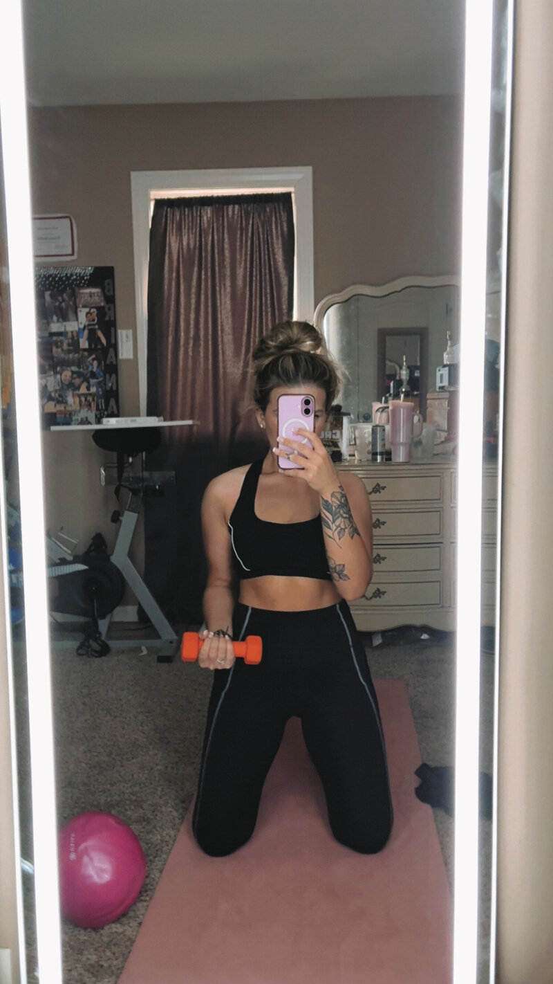 Mirror picture of women taking a picture of her working out with weights 