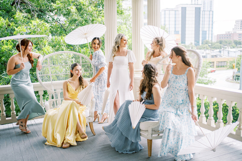 Bride and her bridesmaids sitting on a porch holding parasols taken by Austin wedding photographer