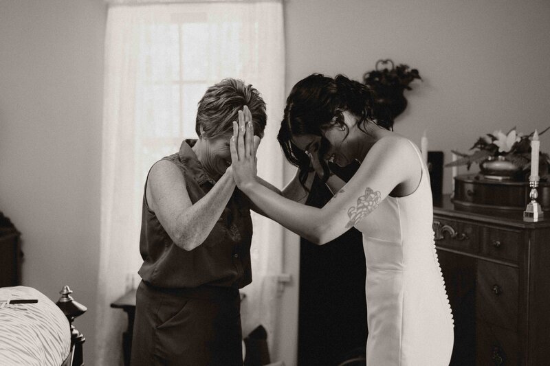 Intimate moment between bride and mother with hands pressed together, both looking down in reflection.