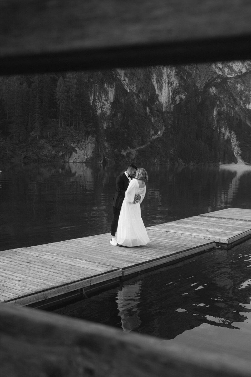 Dolomites elopement | couple stands on a boat dock, with wood rails in the foreground