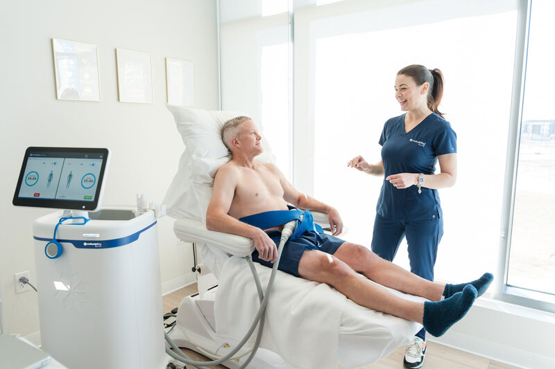 CoolSculpting consultation in Dallas with a male patient lying on a white stretcher. The professional, dressed in a blue uniform, is explaining the treatment and procedure details.