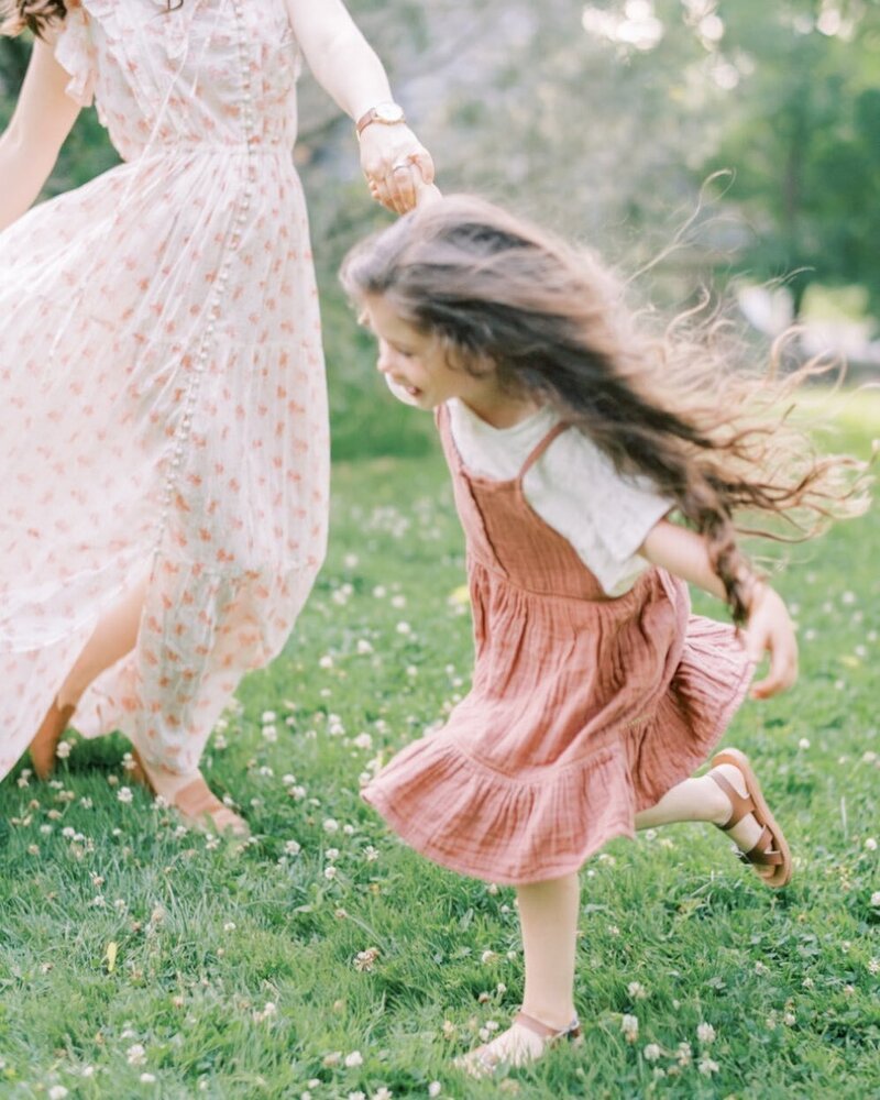 A girl runs, her hair streaming around her, as she holds on to her mother's hand in their sunlit yard. | Pittsburgh Family Photographer | Anna Laero Photography