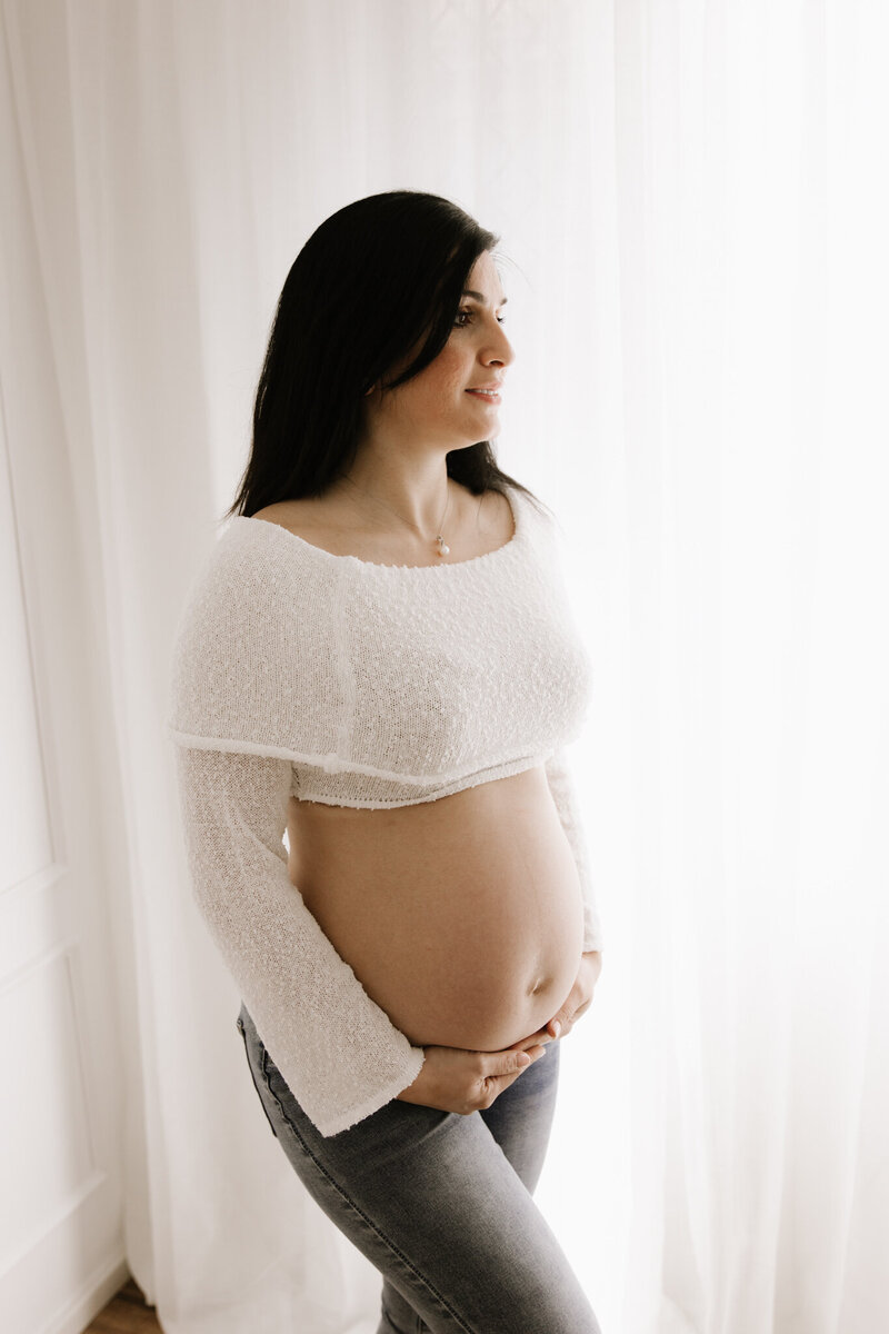 pregnant woman smiles softly while holding her belly during a studio maternity shoot