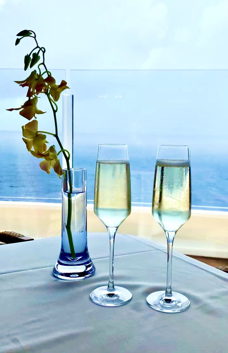 two champagne flutes and vase of flowers overlooking ocean