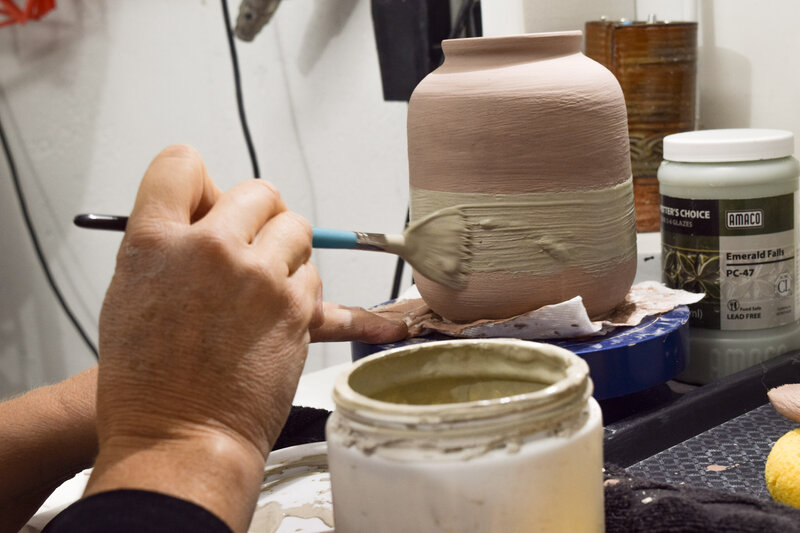 Jill uses a brush to apply glaze on a vase she made. Custom glazes are painted on to create a gradient effect on the finished piece