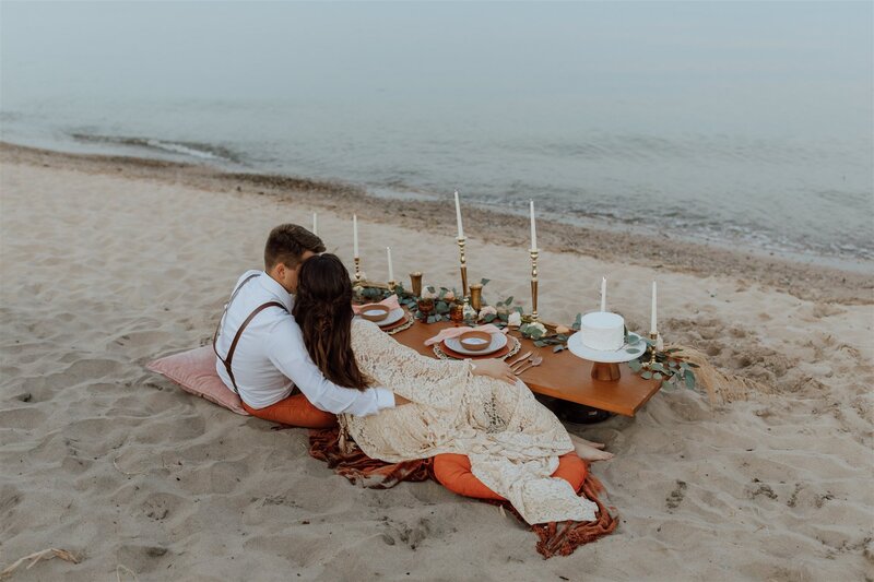 elopement dinner setup on a beach in Wisconsin. Bride and groom are sitting at their table facing the water