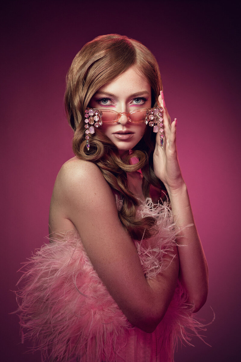 Stylish portrait of Denya in a pink, ruffled outfit with soft curls and bold makeup, captured by Ylva Erevall.