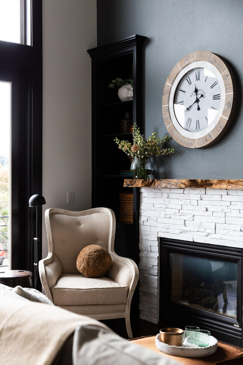 A cozy home corner featuring a beige chair, white brick fireplace, built in bookcase and a large clock.