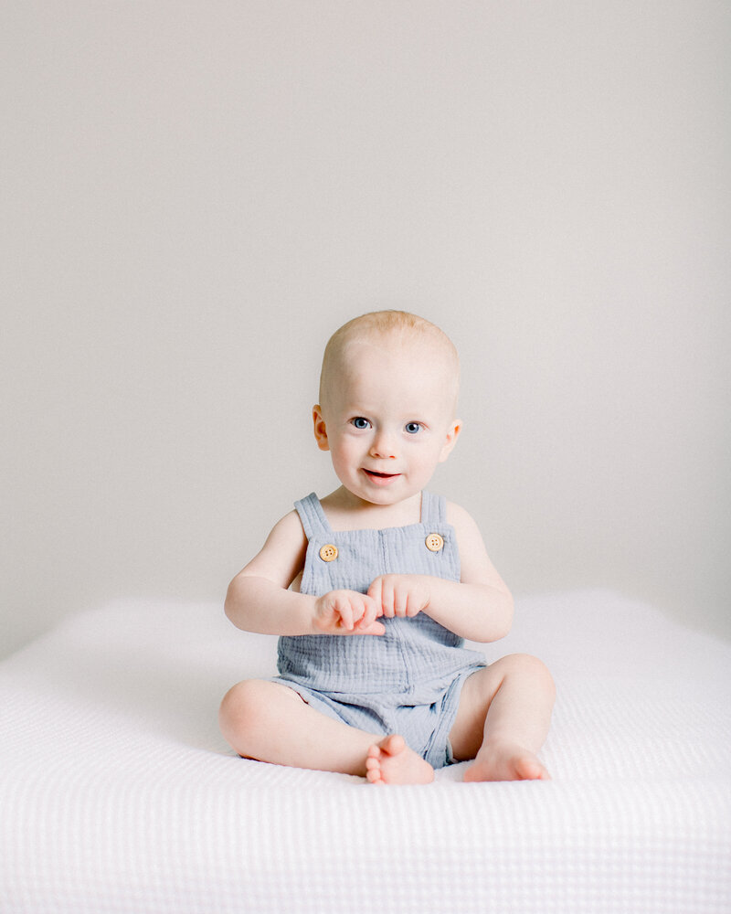 Happy baby holding his hands in a blue romper in neutral nursery by Boston newborn photographer Fieldstone Studio