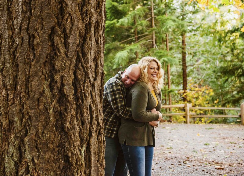 husband and wife hugging in woods beside large tree