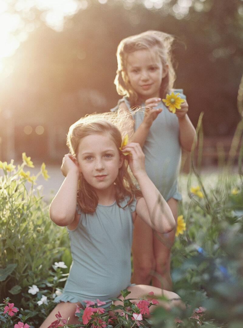 Two little girls in matching swimsuits playing in a butterfly garden while the sun sets behind them in 30A.