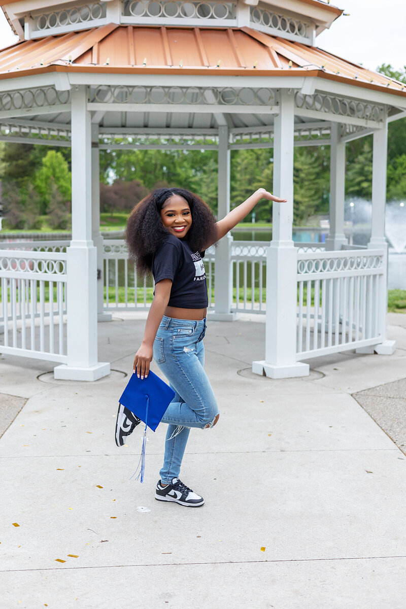 Senior girl holding graduation cap posing in front of a gazebo
