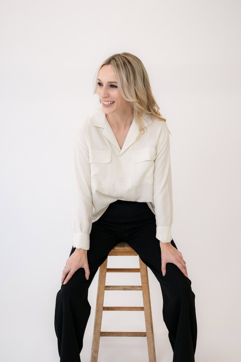 Joy Steele in a professional outfit smiling and sitting on a stool, showcasing the work of a talented Phoenix boudoir photographer.