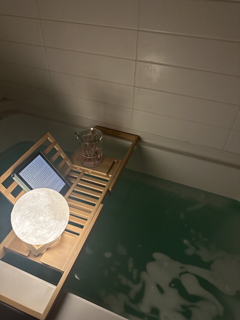 Picture of someone taking a bath while reading a book and having some tea