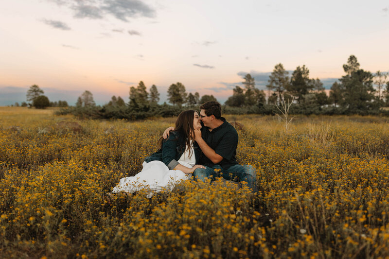 man and women kiss while sitting in a field during their Flagstaff Arizona engagement session