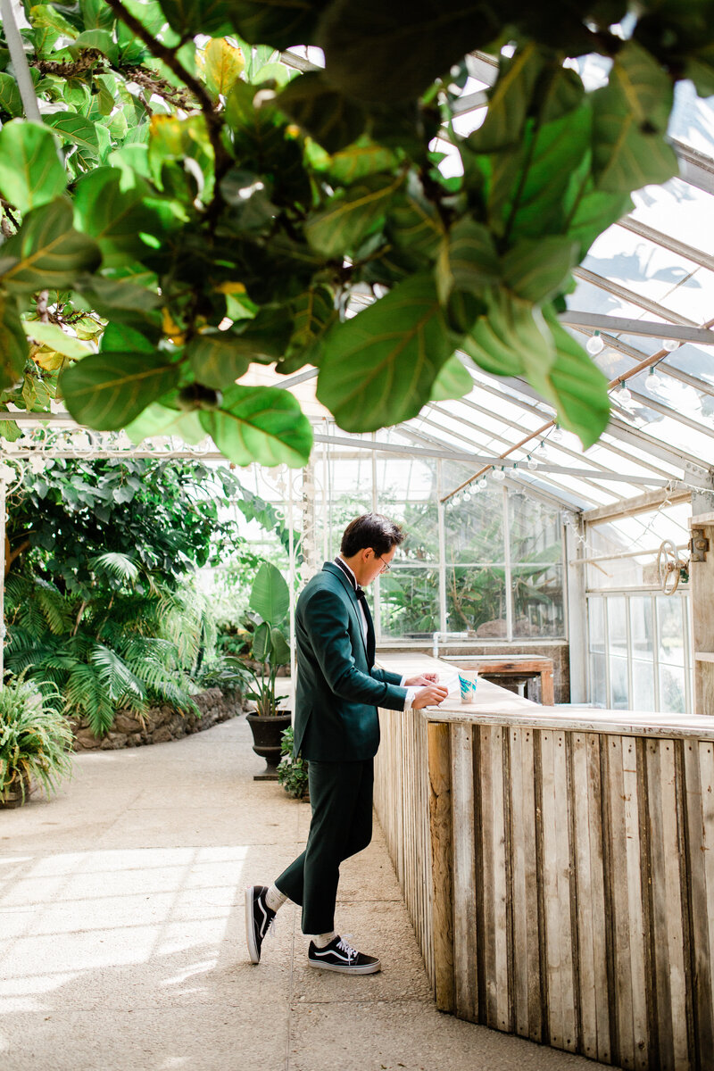 A candid moment of the groom reading over his vows again after getting dressed in his green suit, bowtie, and vans skate shoes.
