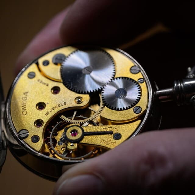 Uhrmacher hält eine geöffnete mechanische Uhr, die das detaillierte Uhrwerk zeigt – ein Zeichen für meisterhafte Handwerkskunst und höchste Präzision.