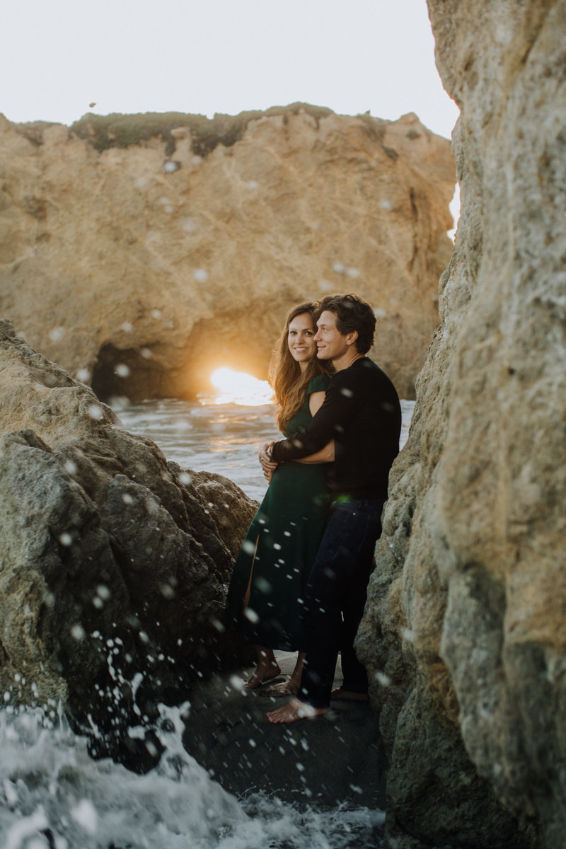 couple leaning up against rocks on the beach