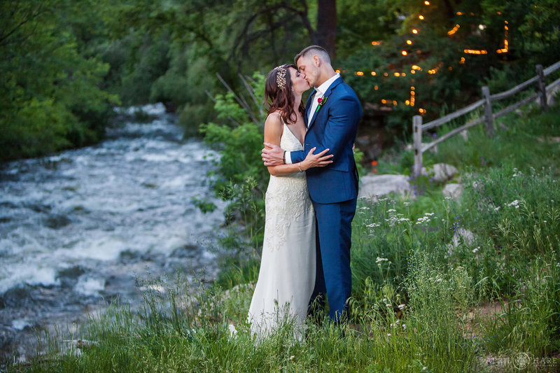 Couple kissing next to Boulder Creek with wildflowers at Wedgewood Weddings in Colorado