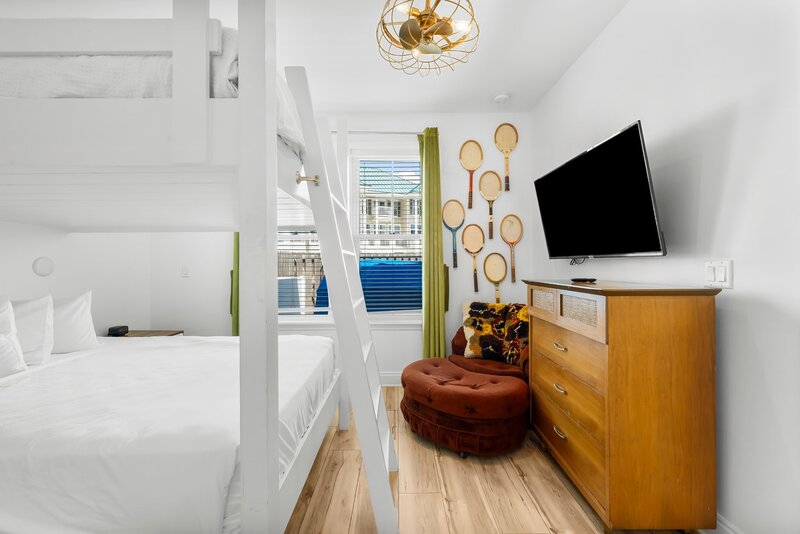 Colorful guest bedroom with mounted TV, vintage decor and bunk bed setup at Groovy Shack in walking distance to Panama City Beach
