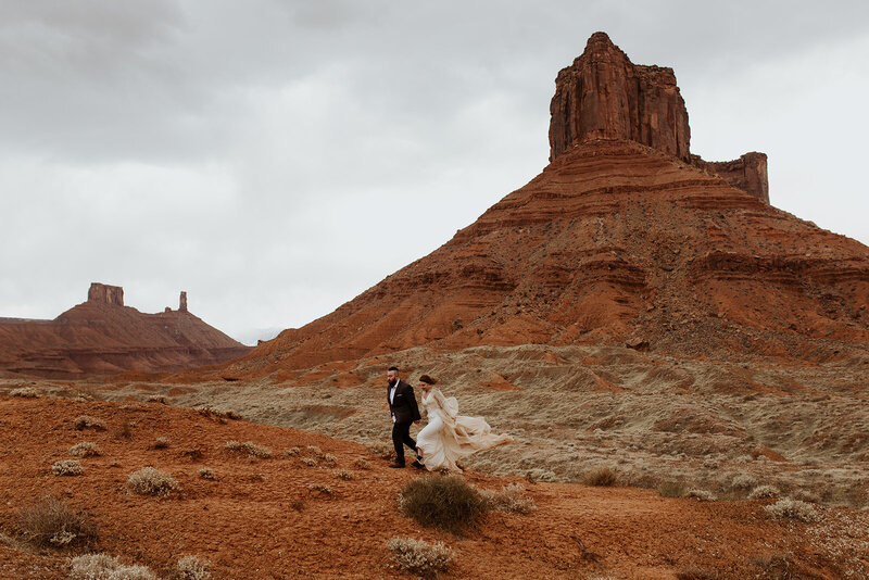 Bride and groom walking in wind swept gown in castle valley, moab, utah