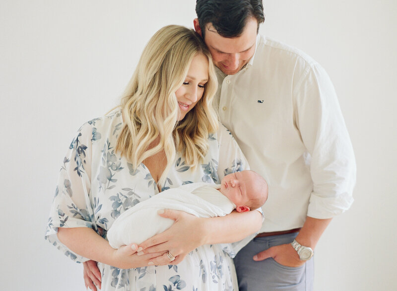 Mom and dad holding a brand new baby boy in an all white studio portrait session in Raleigh. Photographed by Raleigh newborn photographers A.J. Dunlap Photography.