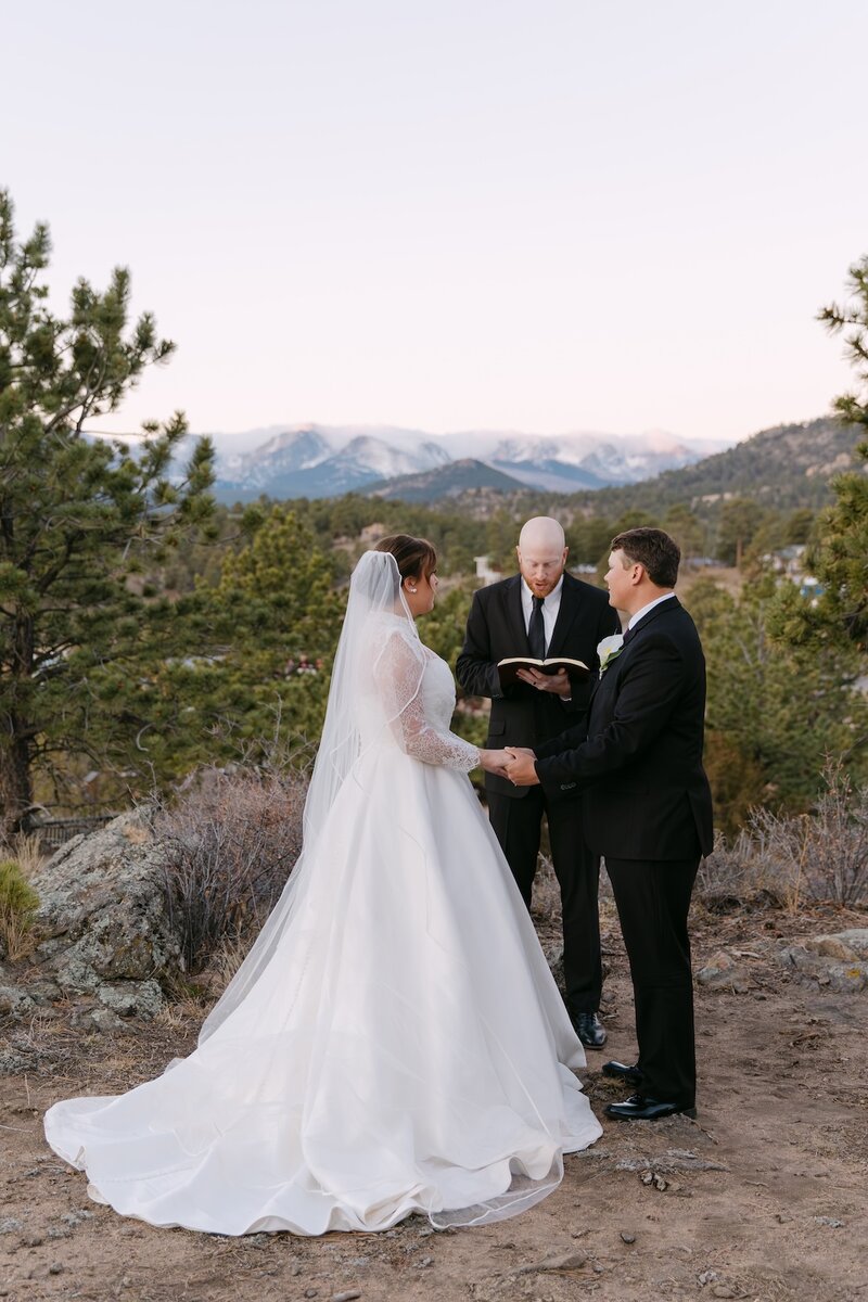 Intimate Colorado micro wedding ceremony with bride and groom and officiant on a rocky overlook with snowcapped mountains in the distance – micro wedding photographer in Colorado