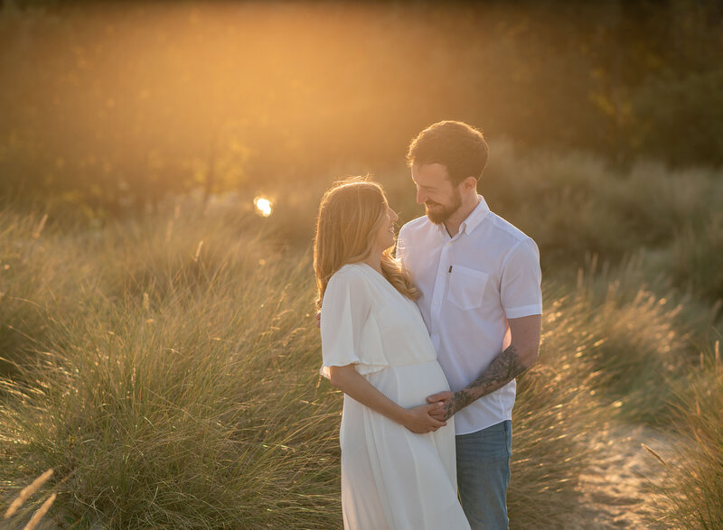 Partner gently cradling bump in warm evening light on a quiet beach in Bournemouth during maternity session