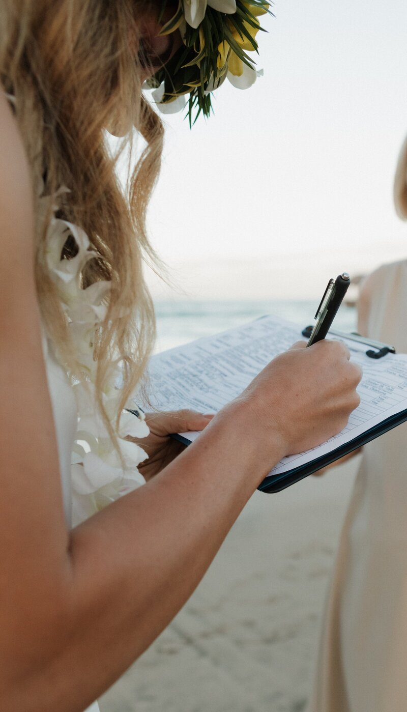 bride on beach signing marriage certificate