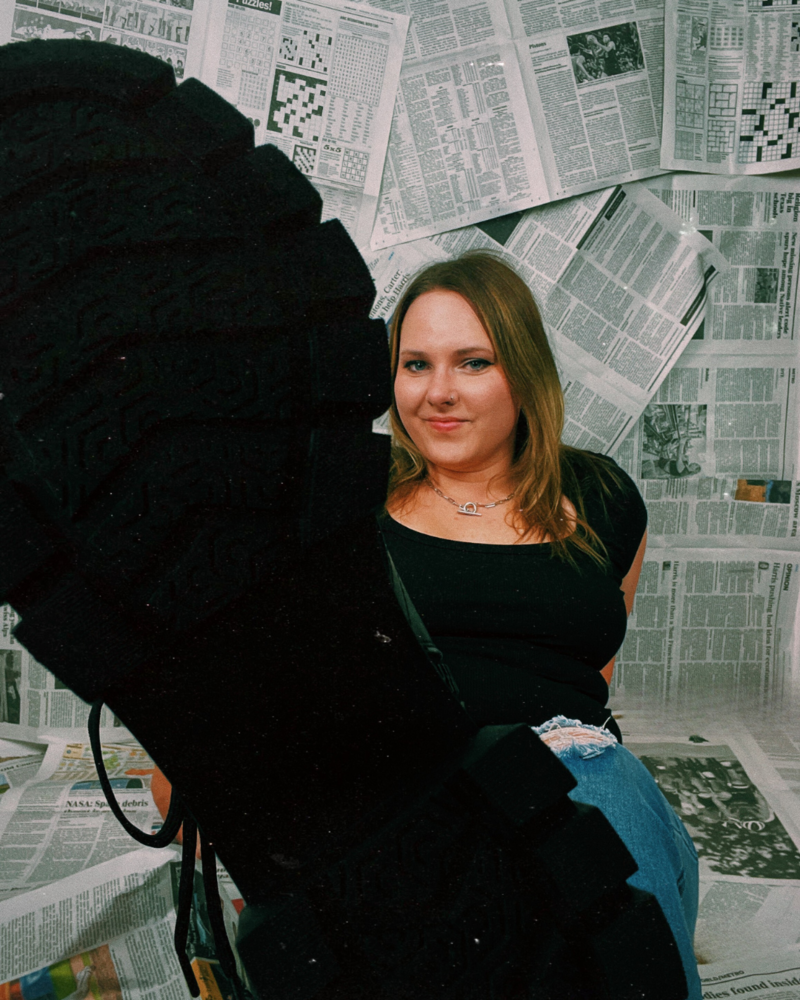 Kristina. a life coach for women, sitting on the floor with a newspaper background, showing bottom of her boot to the camera