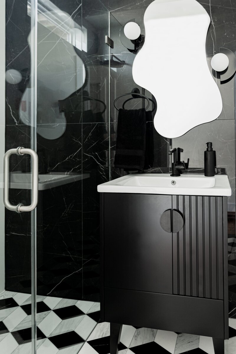 Contemporary bathroom featuring black marble walls, a sleek black vanity with a round mirror, and modern fixtures, creating a luxurious and elegant atmosphere