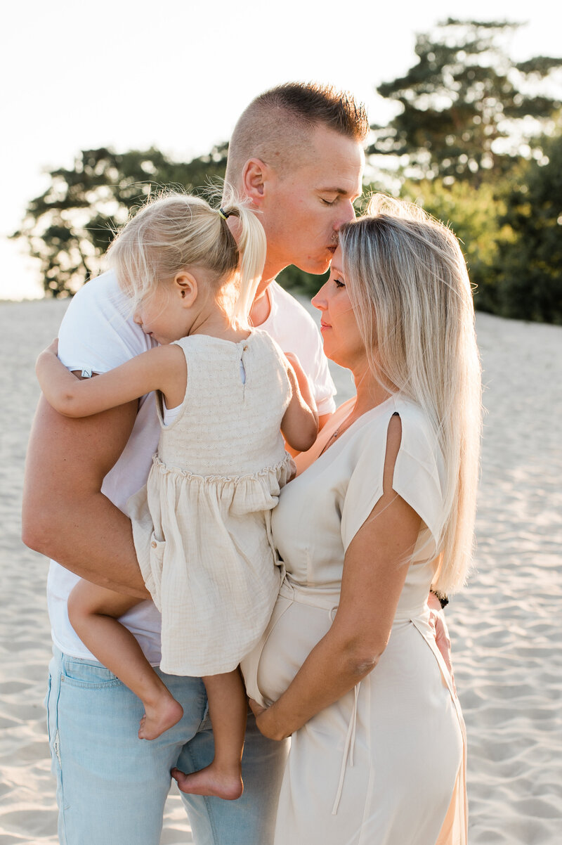 Een zwangerschapsfotoshoot op het strand, waar een moeder liefdevol met haar gezin poseert, gefotografeerd door Monica Stout Fotografie.