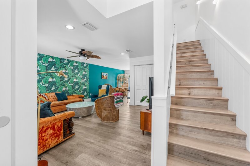 Bright entryway at Tropical House with view into living room, tropical wallpaper, rattan seating, and stairway leading upstairs.