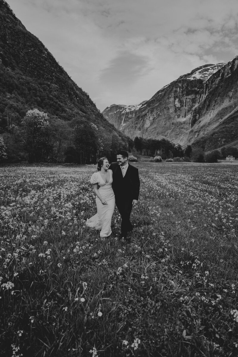 Wedding couple walking an laughing in a field of flowers with big mountain in the background