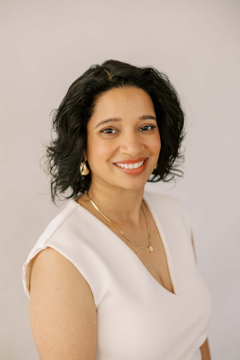 Beautiful Indian woman wearing gold jewelry and an all white outfit and smiling at the camera