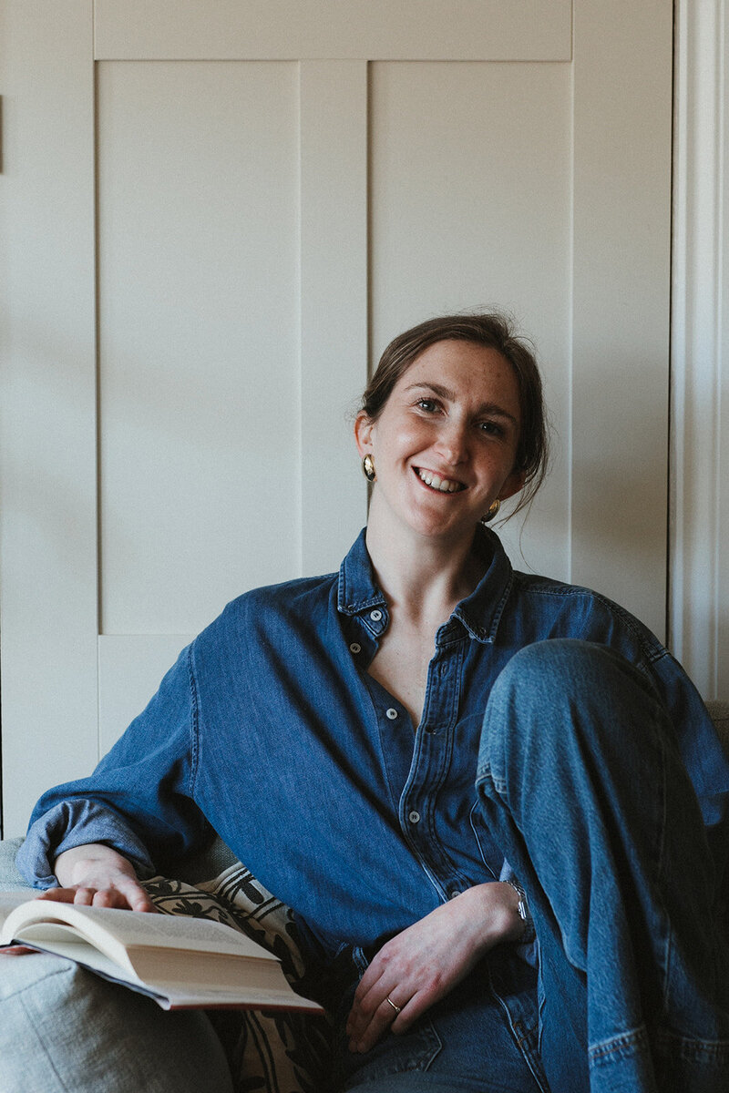 copywriter reading a book on motherhood smiles in her living room in Oxfordshire