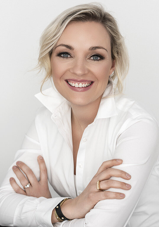 Blonde woman in a white blouse with a radiant smile.