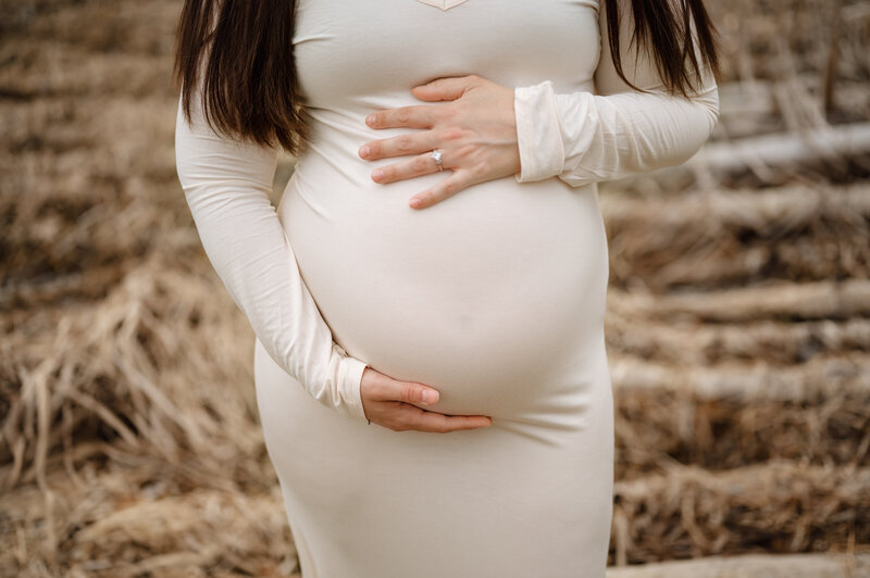 Close-up of an expectant mother in a white dress gently cradling her pregnant belly during a maternity photography session in Grand Rapids, Michigan