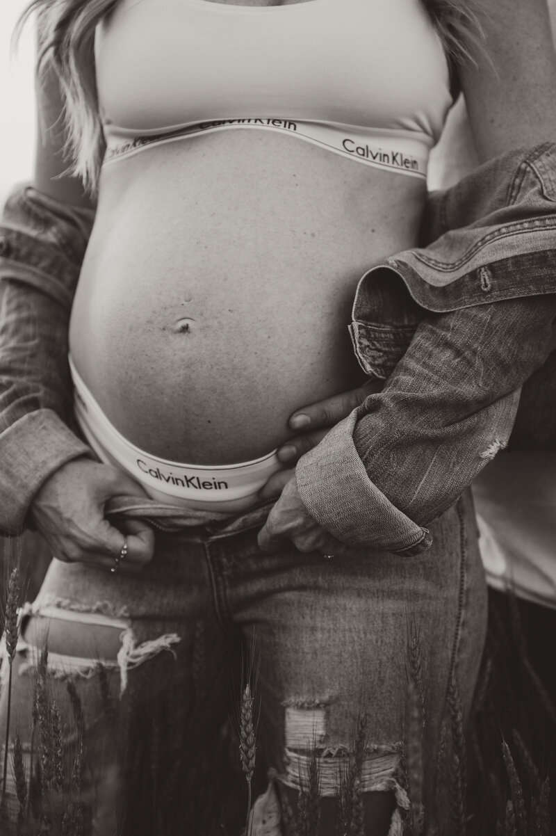 A pregnant mother's belly wearing jeans and calvin clien underwear. 