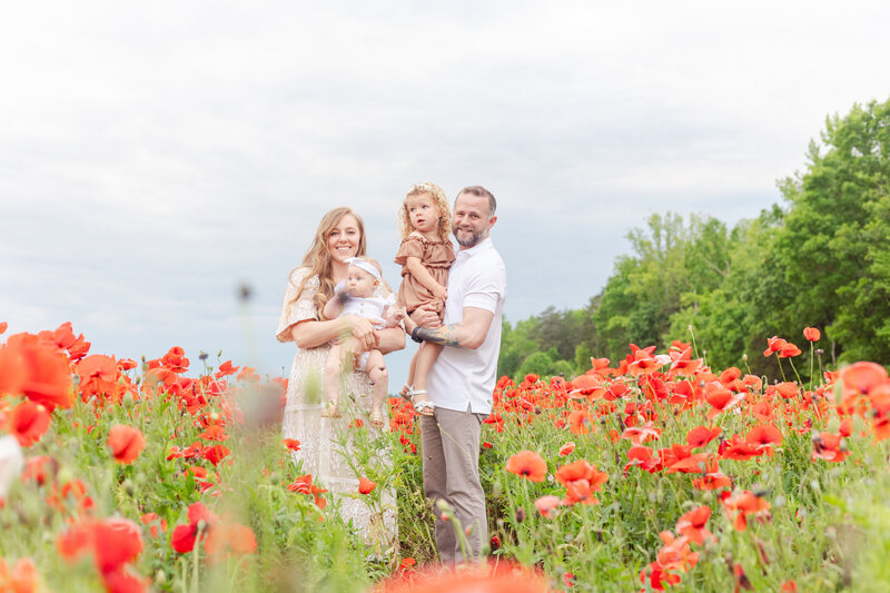 Mom, Dad, and daughters standing in a field full of red poppy flowers