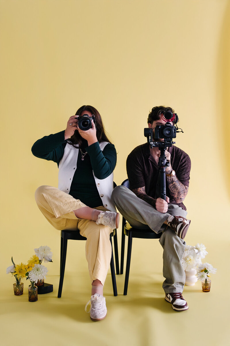 A person sitting on the ground with their partner leans over their shoulders and smiles