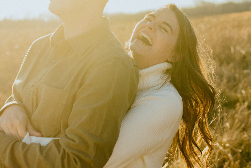 woman hugs man in field sunset engagement 
