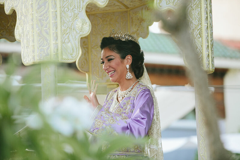 Elegant bride in lavender attire smiling under golden canopy – cultural wedding photography in Morocco