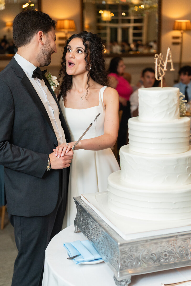 Groom holding a cake knife while the bride looks at him with surprise before cutting their wedding cake