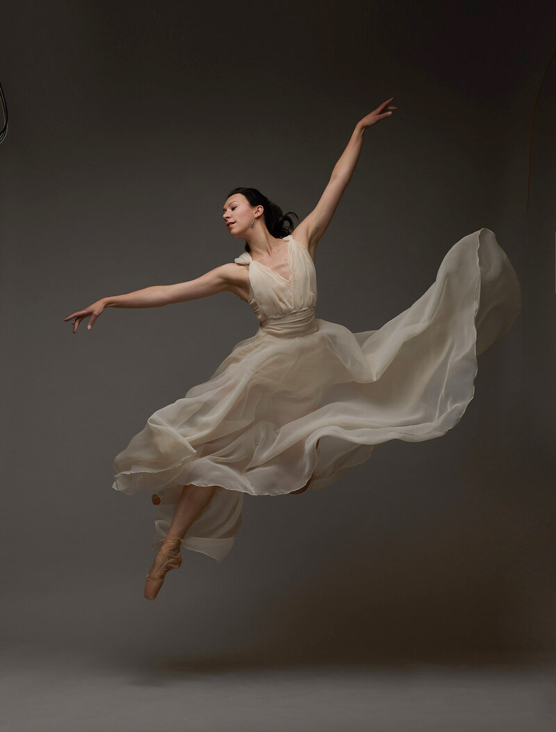 A ballet dancer jumping in the air wearing a flowy gown.