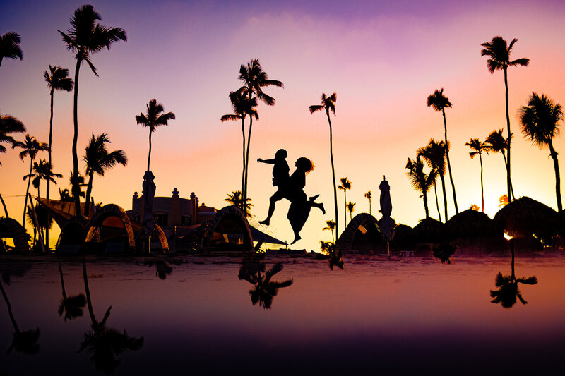 A silhouette of a wedding couple jumping on the beach in Punta Cana with palm trees in the background during sunset