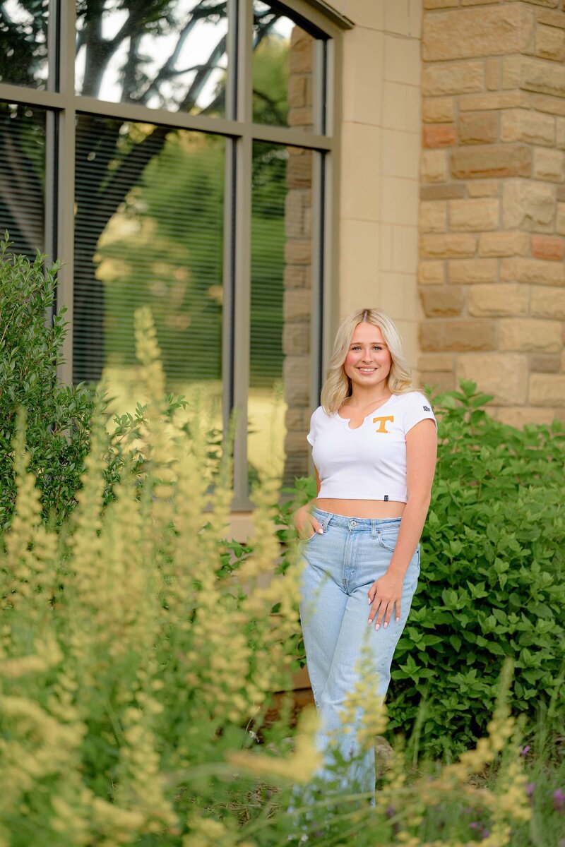 flowers in the foreground of an image showing a blonde senior wearing college gear and jeans during her senior photo session